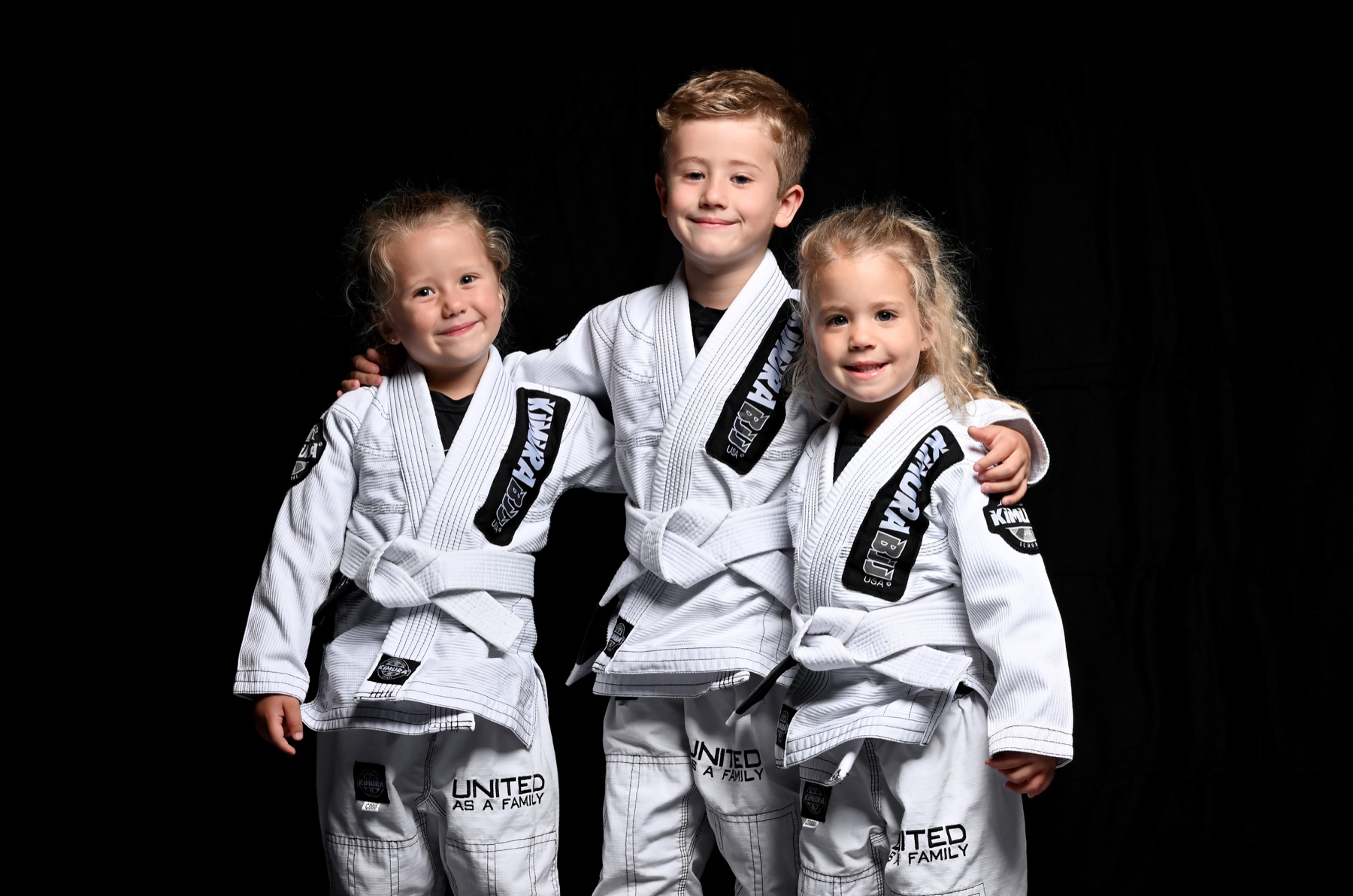 Three siblings in white Jiu-Jitsu gis photographed against a black studio backdrop